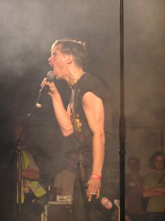 gus gus - der ansager. die &auml;hnlichkeit zu einem uns allen bekannten diktator ist sicherlich gewollt, denn mit den worten "ich bin ein kotzbrocken" parodiert er jenen aufs peinlichste - zu recht, selbstverst&auml;ndlich!!!